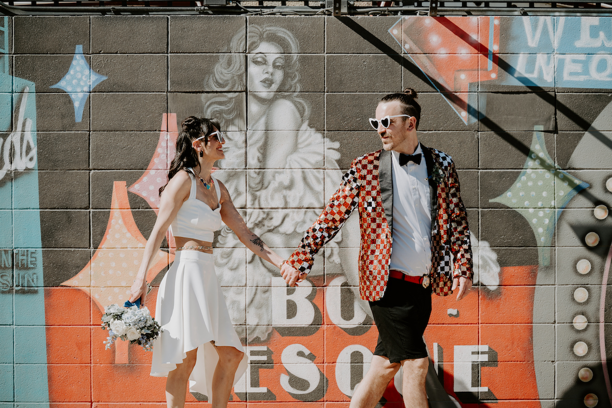 bride and groom in rock-n-roll attire holding hands in front of a mural